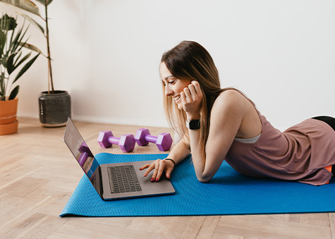 woman laying on yoga mat with laptop