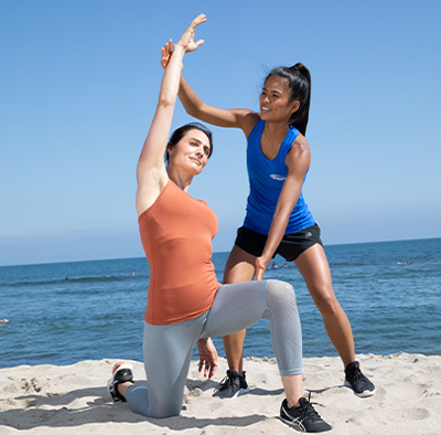 NASM trainer assisting client with lunge stretch on beach