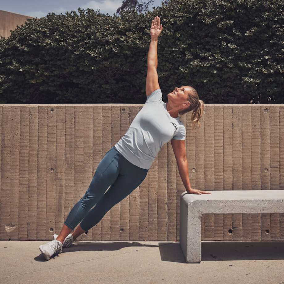 Female NASM trainer doing elevated side plank on cement bench outside