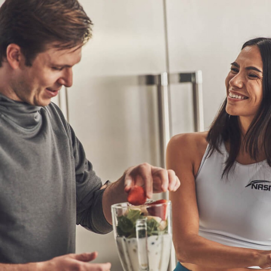 Female Nutrition coach making smoothie with male client in kitchen