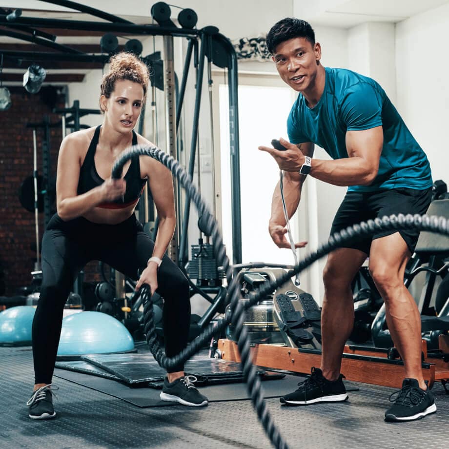 Male trainer assisting female client in rope exercise