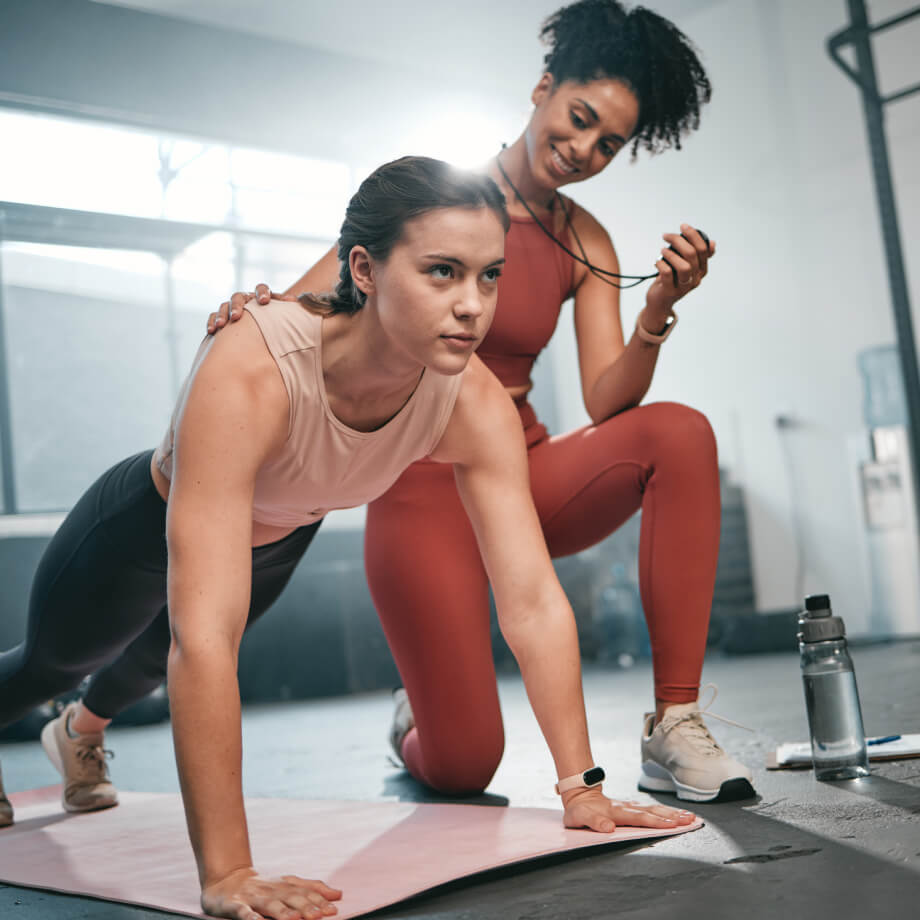 Female trainer assisting female client in plank exercise