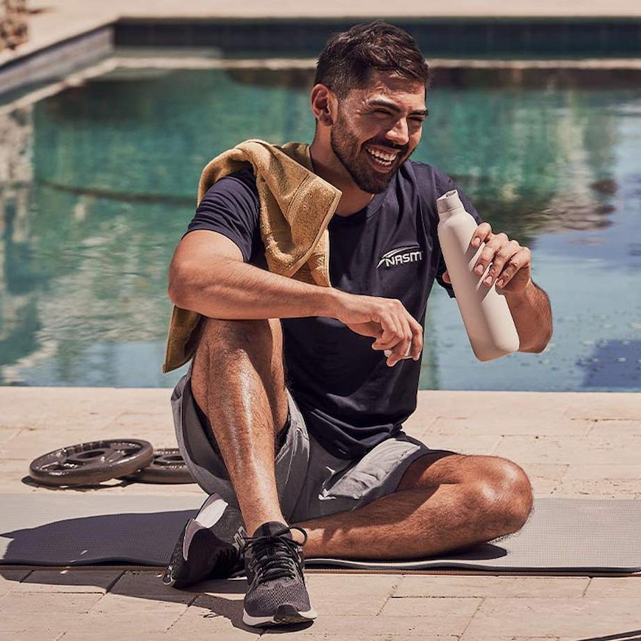 Male NASM trainer drinking water outside